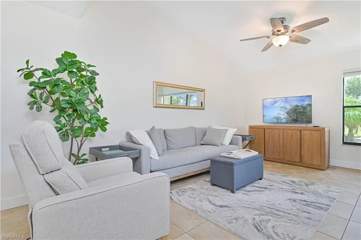 Living room with ceiling fan, light tile patterned floors, and lofted ceiling