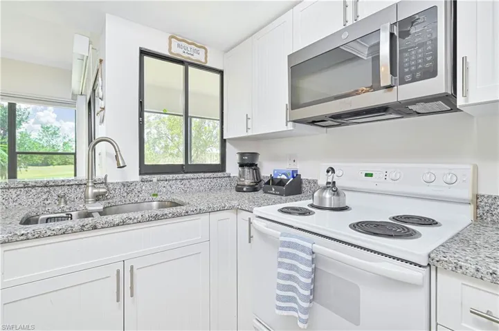 Kitchen with white range with electric stovetop, stainless steel microwave, white cabinetry, and light stone counters