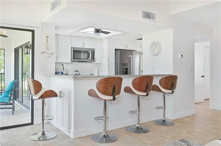 Kitchen featuring a breakfast bar area, stainless steel appliances, light stone countertops, white cabinets, and a ceiling fan