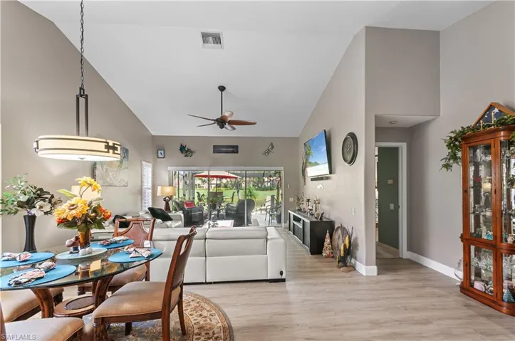Living room featuring high vaulted ceiling, light wood-style flooring, visible vents, baseboards, and a ceiling fan