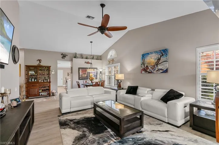 Living area with high vaulted ceiling, visible vents, light wood finished floors, and a ceiling fan