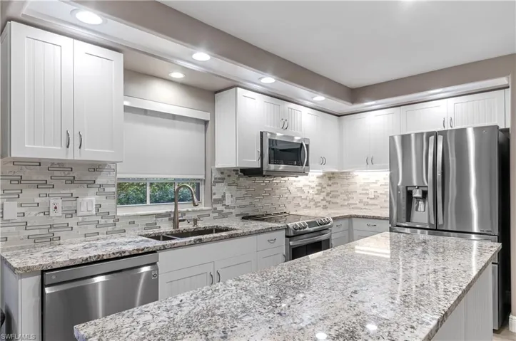 Kitchen with appliances with stainless steel finishes, a sink, light stone countertops, and decorative backsplash