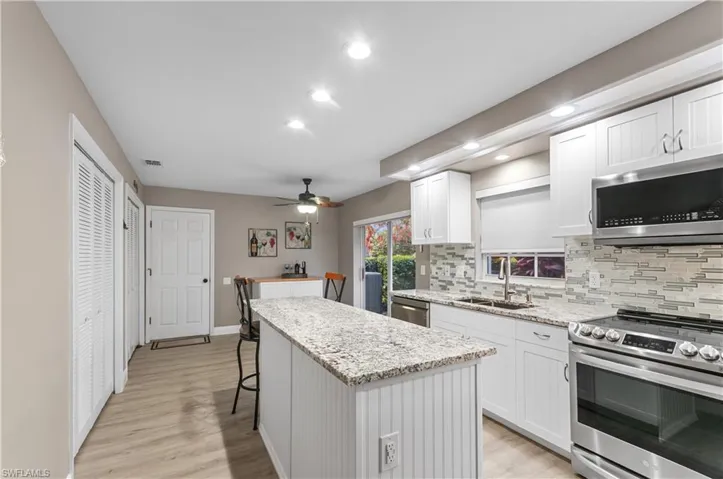 Kitchen with stainless steel appliances, a kitchen island, a sink, white cabinets, and decorative backsplash