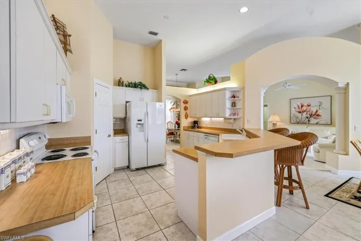 Kitchen with arched walkways, white appliances, a breakfast bar area, and light tile patterned floors