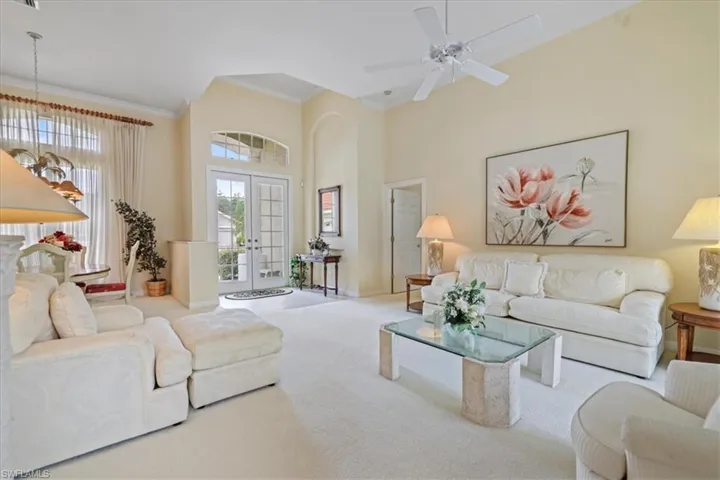 Carpeted living room with french doors, crown molding, a towering ceiling, and baseboards