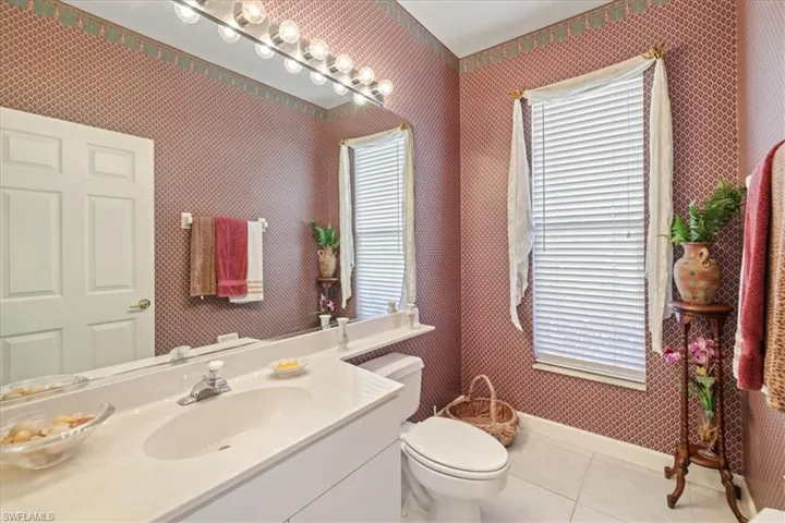 Bathroom with toilet, vanity, tile patterned flooring, baseboards, and wallpapered walls