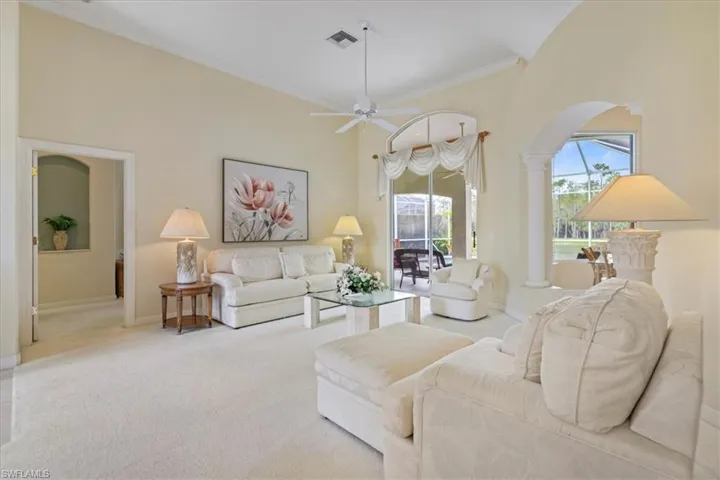 Carpeted living room with a towering ceiling, ornate columns, baseboards, and crown molding