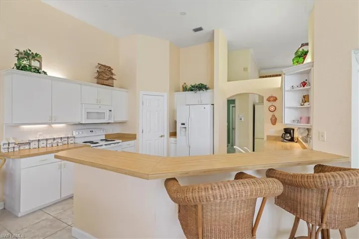 Kitchen with light tile patterned flooring, a peninsula, white appliances, white cabinetry, and light countertops