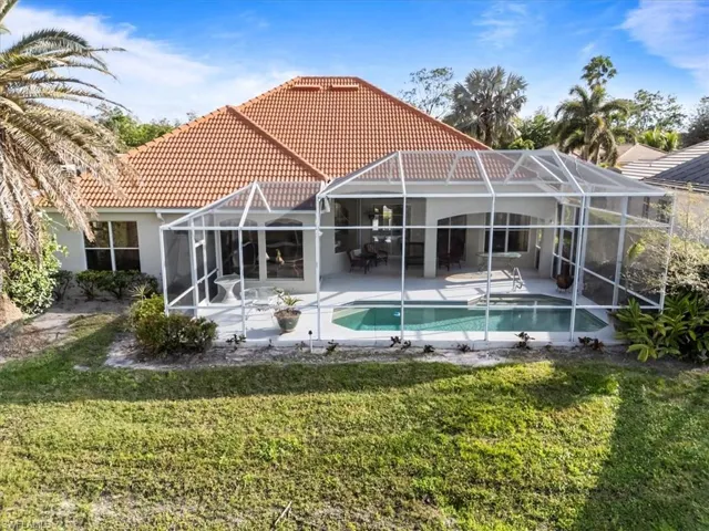 Back of house with glass enclosure, a tile roof, a lawn, and a patio