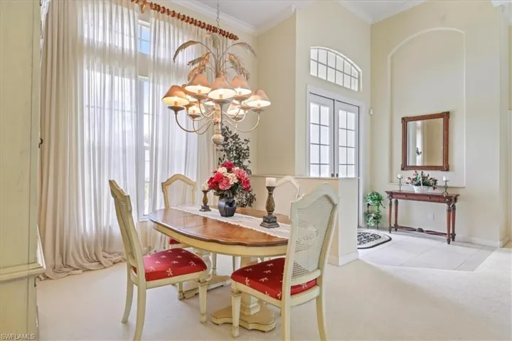 Dining space with a notable chandelier, a high ceiling, baseboards, carpet, and crown molding
