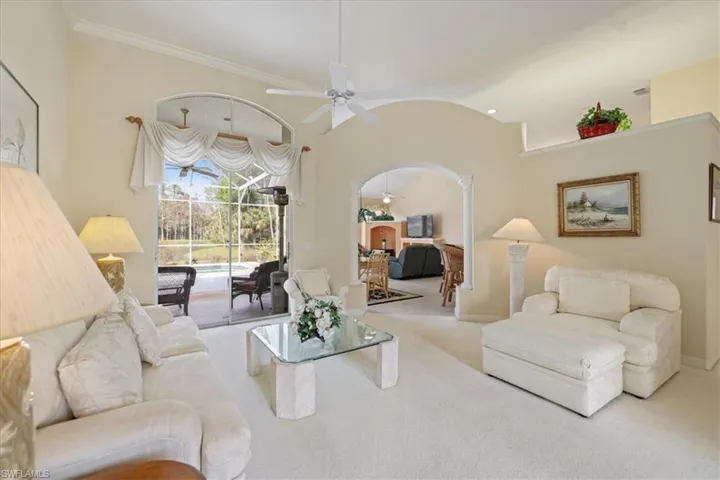 Carpeted living area with arched walkways, a ceiling fan, baseboards, vaulted ceiling, and crown molding