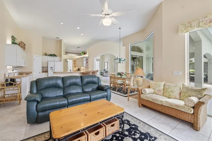 Living area featuring light tile patterned floors, arched walkways, ceiling fan with notable chandelier, high vaulted ceiling, and recessed lighting