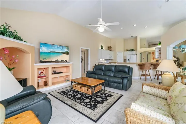Living room with a ceiling fan, arched walkways, light tile patterned flooring, and vaulted ceiling