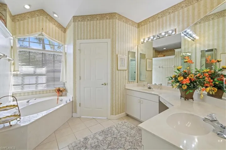 Bathroom featuring tile patterned flooring, a sink, a bath, and wallpapered walls