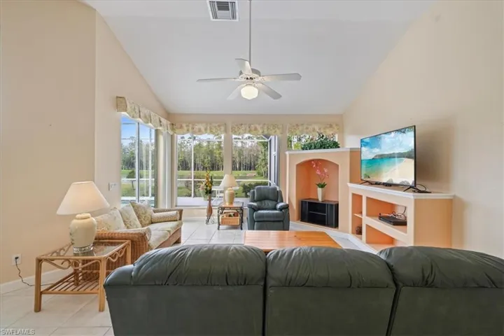Living room featuring ceiling fan, light tile patterned flooring, visible vents, baseboards, and vaulted ceiling