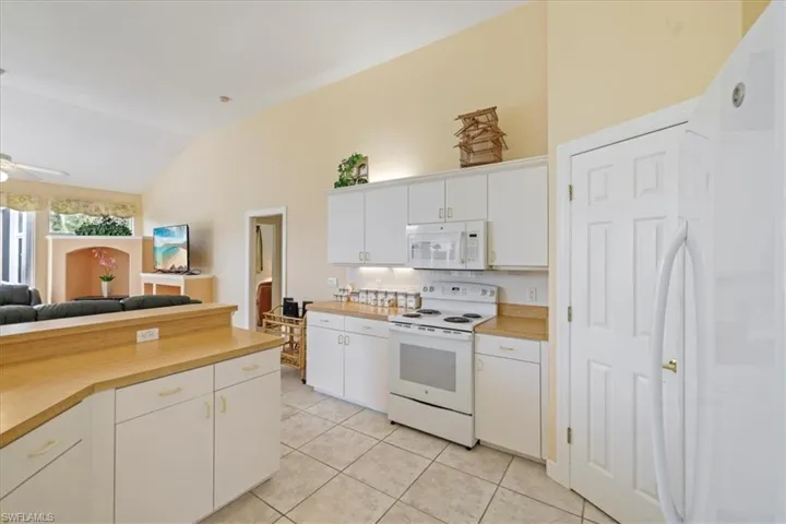 Kitchen with white appliances, white cabinets, open floor plan, vaulted ceiling, and light tile patterned flooring
