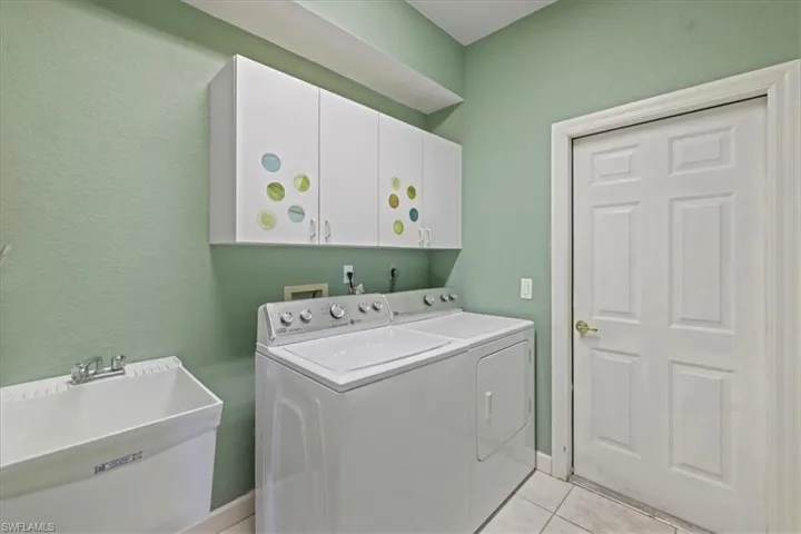 Laundry room with cabinet space, light tile patterned floors, washer and dryer, and a sink
