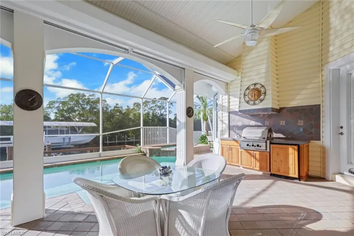 Covered outdoor dining area with built-in grill overlooking the pool.