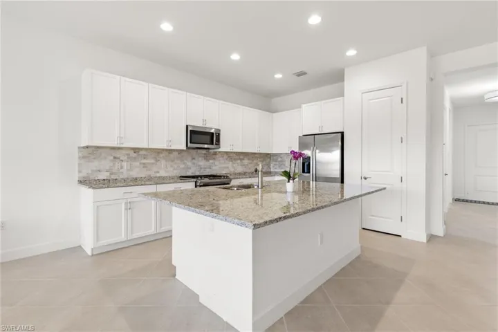 Kitchen with sink, decorative backsplash, light stone counters, stainless steel appliances, and a center island with sink