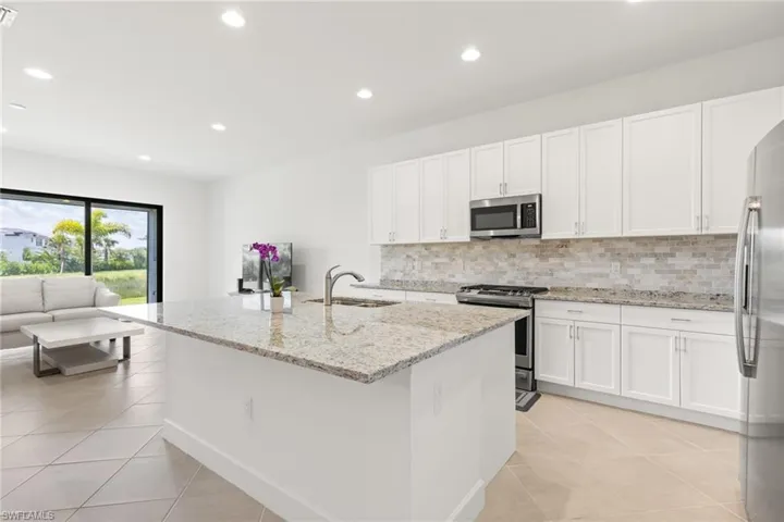 Kitchen featuring light tile patterned flooring, sink, decorative backsplash, stainless steel appliances, and white cabinets