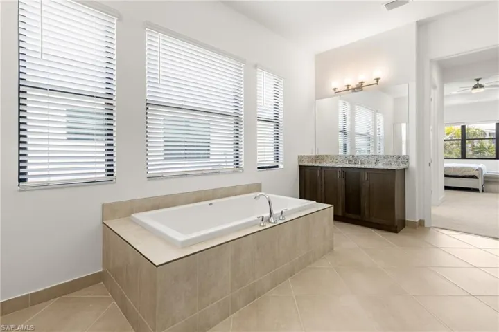 Bathroom with tile patterned floors, vanity, a relaxing tiled tub, and ceiling fan