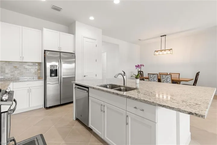 Kitchen featuring backsplash, stainless steel appliances, sink, a center island with sink, and light tile patterned floors