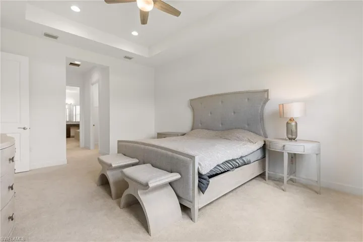 Carpeted bedroom featuring ceiling fan and a tray ceiling