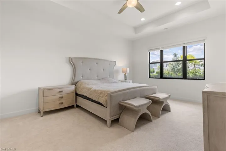 Bedroom featuring ceiling fan, light carpet, and a tray ceiling
