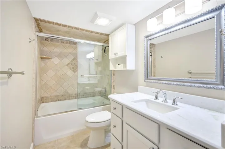 Bathroom featuring bath / shower combo with glass door, vanity, and light tile patterned flooring