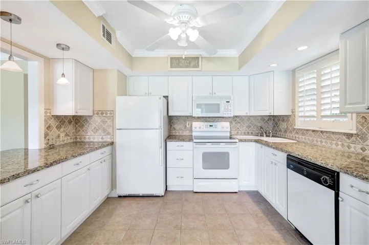 Kitchen with ornamental molding, white appliances, white cabinetry, backsplash, and light stone countertops