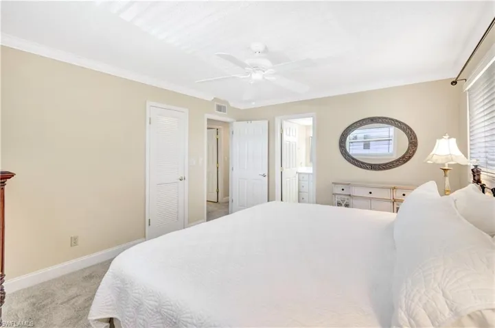 Bedroom with light colored carpet, ornamental molding, ceiling fan, connected bathroom, and a closet