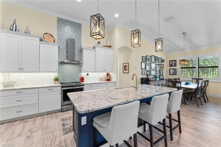 Kitchen featuring all wood all American made cabinetry, electric range, an island with sink, and wall chimney exhaust hood.