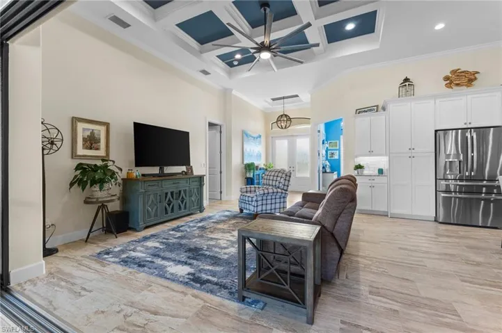 Living room featuring a towering ceiling, ornamental molding, coffered ceiling, ceiling fan, and beam ceiling
