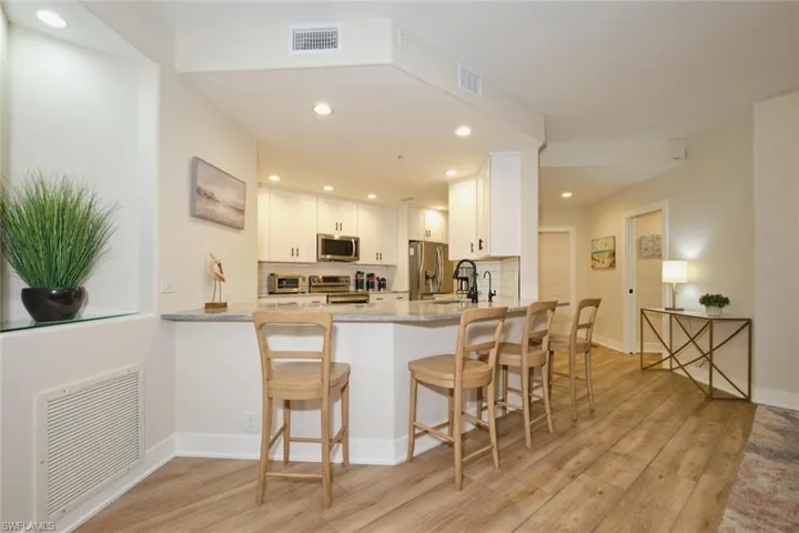 Kitchen featuring white cabinetry, kitchen peninsula, stainless steel appliances, light stone counters, and decorative backsplash