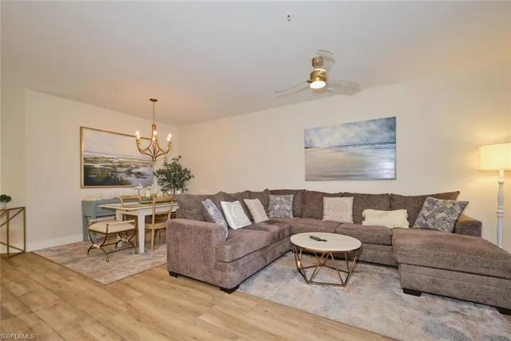 Living room featuring ceiling fan with notable chandelier and wood-type flooring