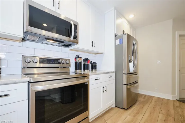 Kitchen featuring white cabinets, light hardwood / wood-style flooring, stainless steel appliances, and light stone counters