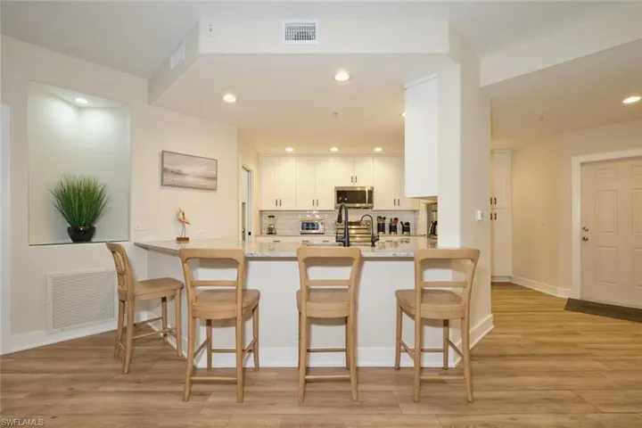 Kitchen featuring appliances with stainless steel finishes, a breakfast bar, white cabinetry, kitchen peninsula, and decorative backsplash