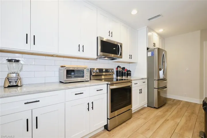 Kitchen with stainless steel appliances, light hardwood / wood-style flooring, light stone counters, white cabinets, and decorative backsplash