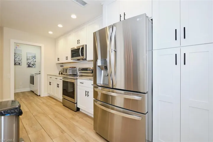 Kitchen with appliances with stainless steel finishes, backsplash, light wood-type flooring, white cabinetry, and separate washer and dryer