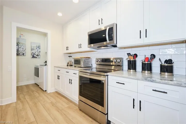 Kitchen with appliances with stainless steel finishes, washing machine and dryer, white cabinets, light stone countertops, and decorative backsplash