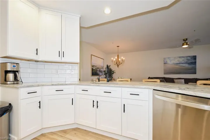 Kitchen featuring light stone counters, white cabinets, stainless steel dishwasher, backsplash, and sink