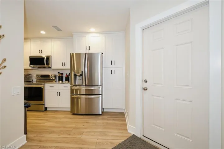Kitchen featuring light wood-type flooring, appliances with stainless steel finishes, white cabinets, and decorative backsplash