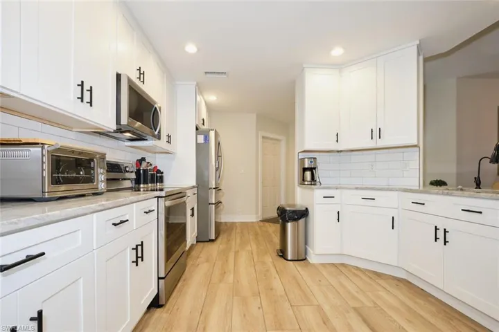 Kitchen featuring light hardwood / wood-style flooring, light stone counters, stainless steel appliances, white cabinets, and decorative backsplash