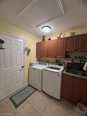 Laundry room featuring separate washer and dryer, light tile patterned flooring, sink, and cabinets