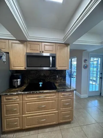Kitchen with dark stone counters, black cooktop, ornamental molding, and tasteful backsplash