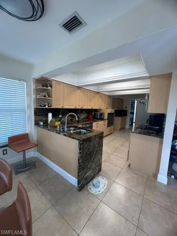 Kitchen with tasteful backsplash, sink, light brown cabinets, light tile patterned floors, and black oven
