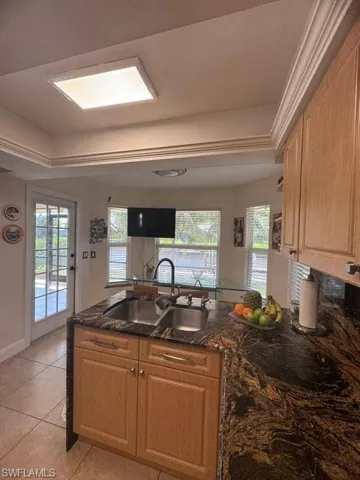 Kitchen with dark stone countertops, light tile patterned flooring, sink, and a healthy amount of sunlight
