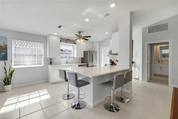 Kitchen with a peninsula, a kitchen bar, ceiling fan, white cabinetry, and backsplash