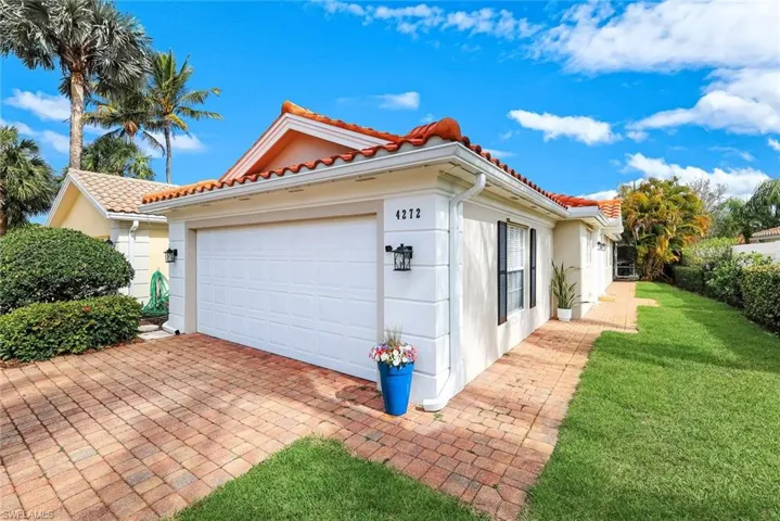 View of side of home with a tile roof, a garage, stucco siding, and a lawn