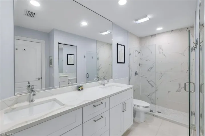 Full bathroom featuring double vanity, a marble finish shower, and recessed lighting